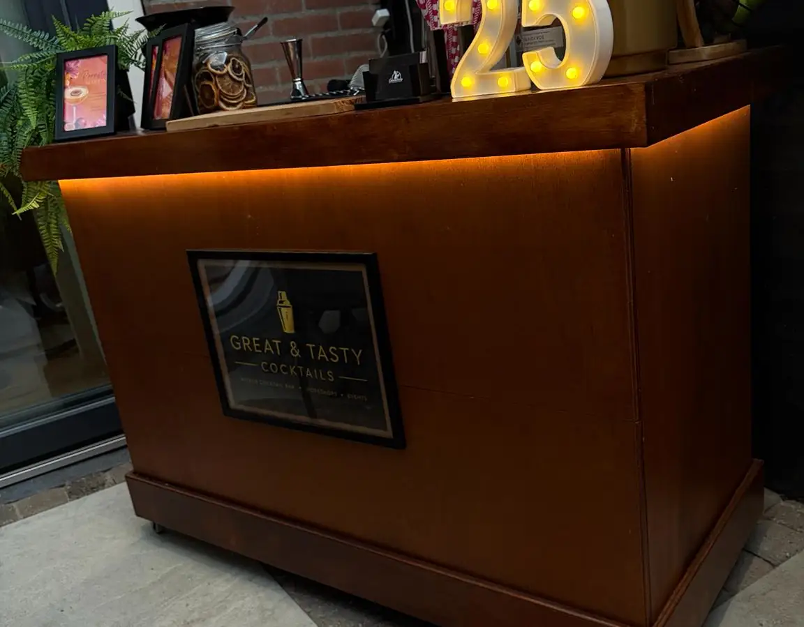 De mobiele bar van Great & Tasty in de schemer, met de verlichting onder het werkblad aan en het logo achter glas