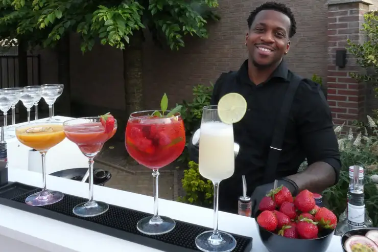 Rudy achter zijn bar, met vier afgemaakte cocktails op de barmat voor hem